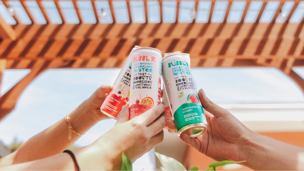 Close-up of three hands cheersing cans of BUBBL'R sparkling water