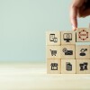 Image of a person's hand stacking 9 wooden blocks in a square and the primary block says "omni."