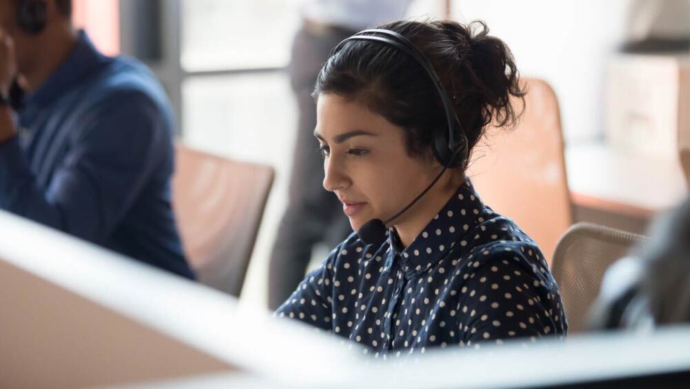 Lady with a headset on sitting at a desk.