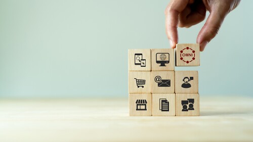 Image of a person's hand stacking 9 wooden blocks in a square and the primary block says "omni."